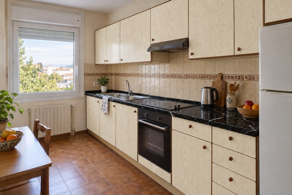 Cuisine des années 1980 sur un mur, façades en chêne pâle, plan de travail effet marbre noir veiné de blanc, carrelage à frise gardé. Façades Pale Oak AG13, plan de travail Nero Marquina U50. Image d'ambiance aux teintes du catalogue.